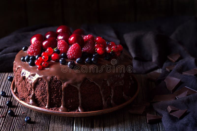 Traditional homemade chocolate cake sweet pastry dessert with brown icing, cherries, raspberry, currant on vintage wooden background. Dark food photo, rustic style, natural light. Traditional homemade chocolate cake sweet pastry dessert with brown icing, cherries, raspberry, currant on vintage wooden background. Dark food photo, rustic style, natural light.