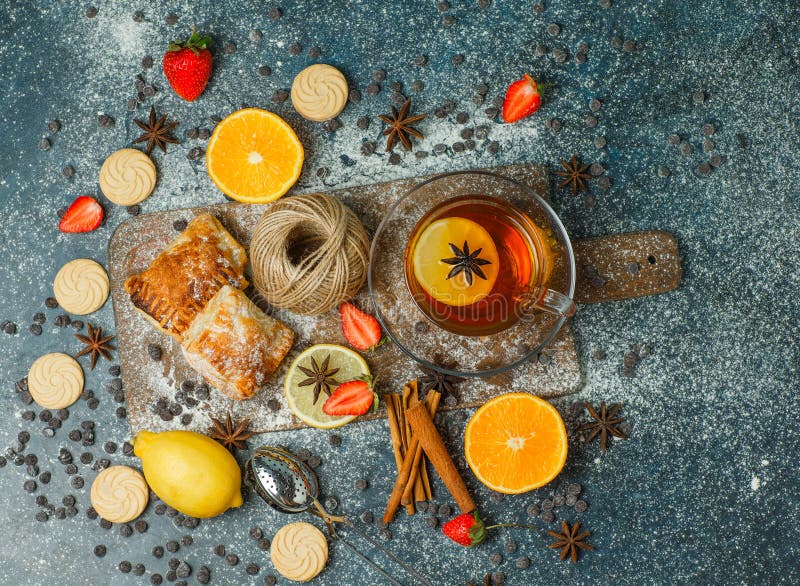 Pastries with flour, tea, fruits, cookies, choco chips, spices, thread on stucco and cutting board background, top view
