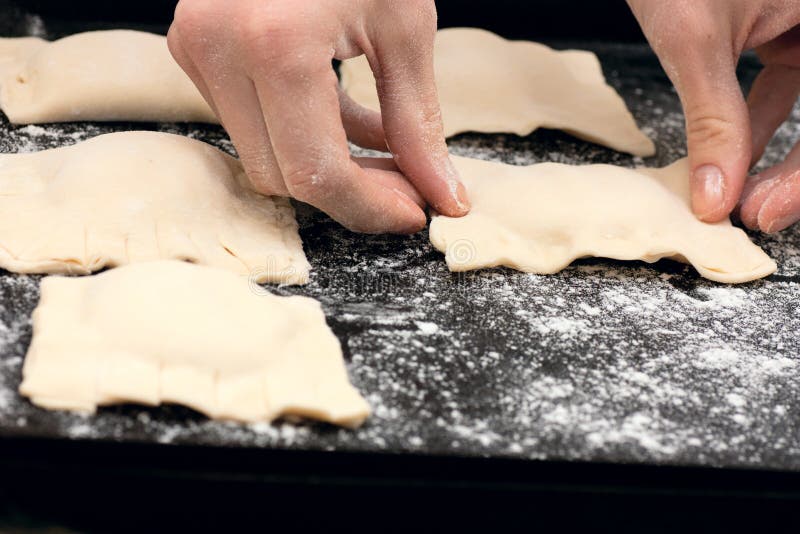 Pair of hands laying out raw pastries on a baking tray. Pair of hands laying out raw pastries on a baking tray