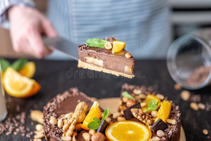 Pastry chef in hand holding a piece of chocolate cake with orange and peanuts. Healthy raw desserts for vegan food