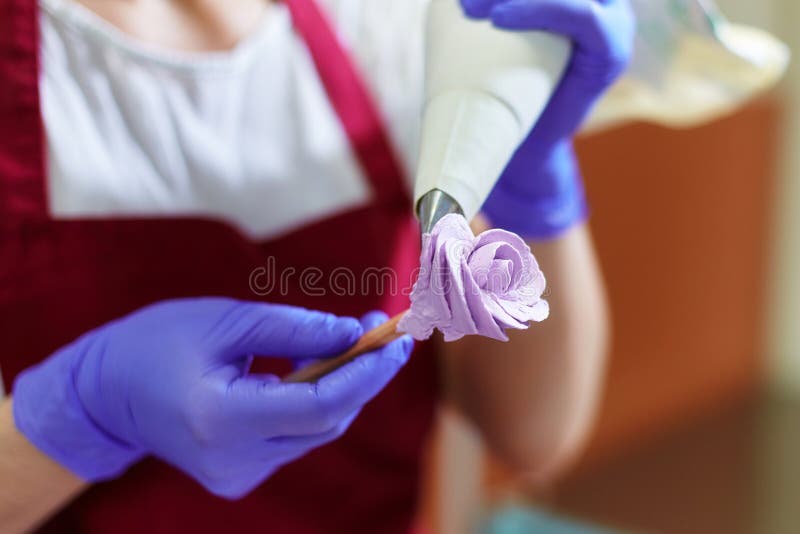 The pastry chef makes a rose flower out of buttercream to decorate the cake. The cream is squeezed out of the pastry bag through a