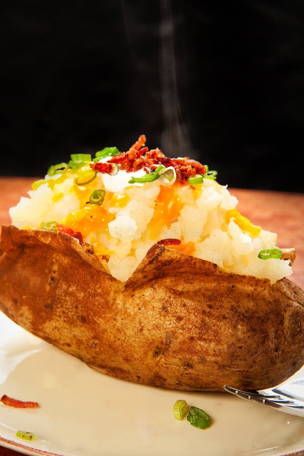 Steaming baked potato loaded with cheese, green onion, sour cream, and bacon. Steaming baked potato loaded with cheese, green onion, sour cream, and bacon