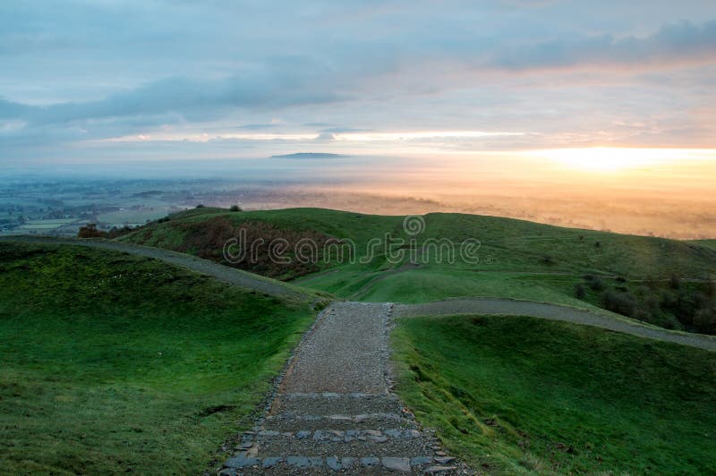 A path heading into the downhill. On the iron age hill fort of British Camp, Malvern Hills. With the the sun rising on a misty mor