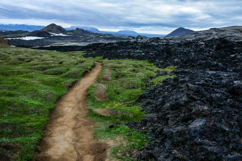 Path to Leirhnjukur old black lava field with colorful stones and smoke coming from ground and blue sky in Iceland, overcast day