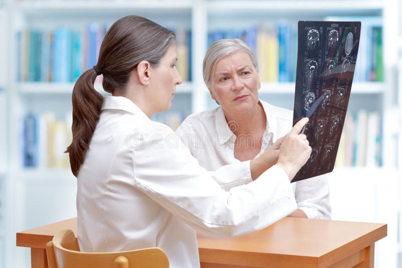 Female middle aged doctor discussing with her senior stroke patient ct-scan images of her brain. Female middle aged doctor discussing with her senior stroke patient ct-scan images of her brain