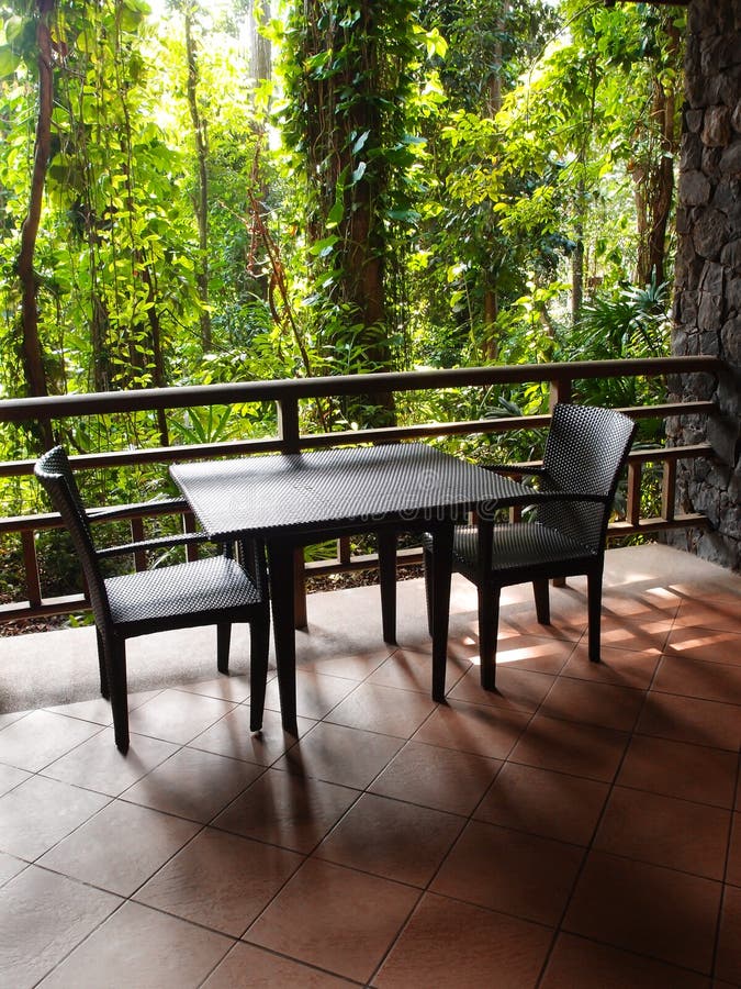 A photograph showing a patio or veranda area of an eco tourism resort hotel, with a beautiful green view of the surrounding tropics jungle. Colour scheme is natural and subtle, and furniture on patio is made of natural materials such as wood timber, bamboo and rattan cane. Natural eco architectural theme. Contemporary and simple modern interior design decor style with natural zen elements close to nature. Vertical format image, nobody in picture. A photograph showing a patio or veranda area of an eco tourism resort hotel, with a beautiful green view of the surrounding tropics jungle. Colour scheme is natural and subtle, and furniture on patio is made of natural materials such as wood timber, bamboo and rattan cane. Natural eco architectural theme. Contemporary and simple modern interior design decor style with natural zen elements close to nature. Vertical format image, nobody in picture.