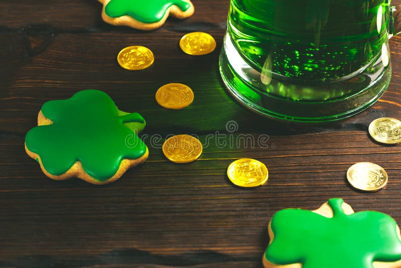 Patrick`s day background with a Glass of green beer and clover gingerbread with gold coins on wooden stock images Patrick`s day background with a Glass of green beer and clover gingerbread with gold coins on wooden stock images