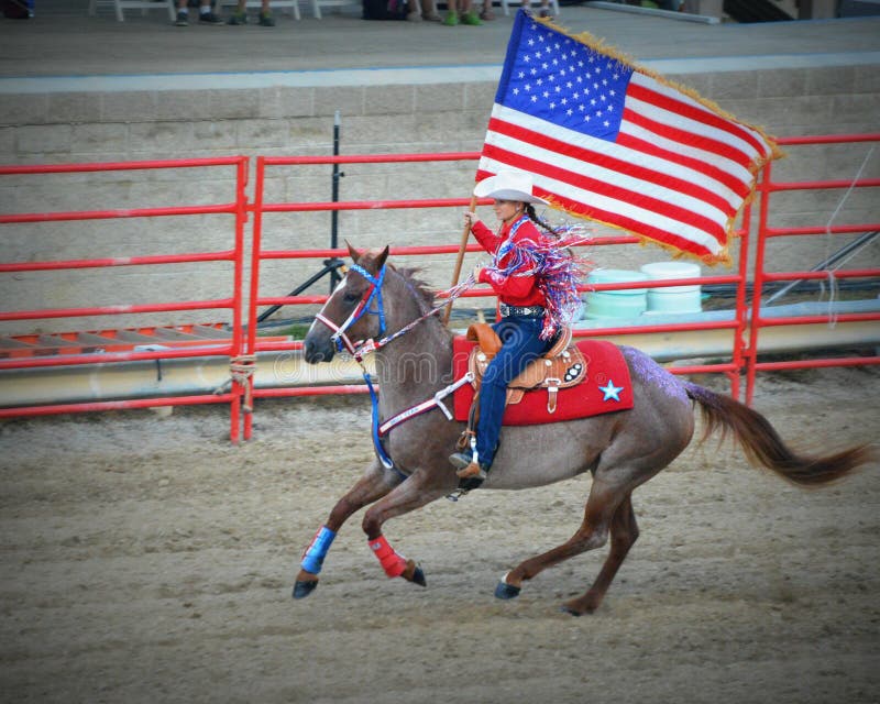 A patriotic cowgirl riding on horseback carrying an American Flag for the National Anthem during the rodeo at the Walworth County Fair, located in Elkhorn, WI. A patriotic cowgirl riding on horseback carrying an American Flag for the National Anthem during the rodeo at the Walworth County Fair, located in Elkhorn, WI.