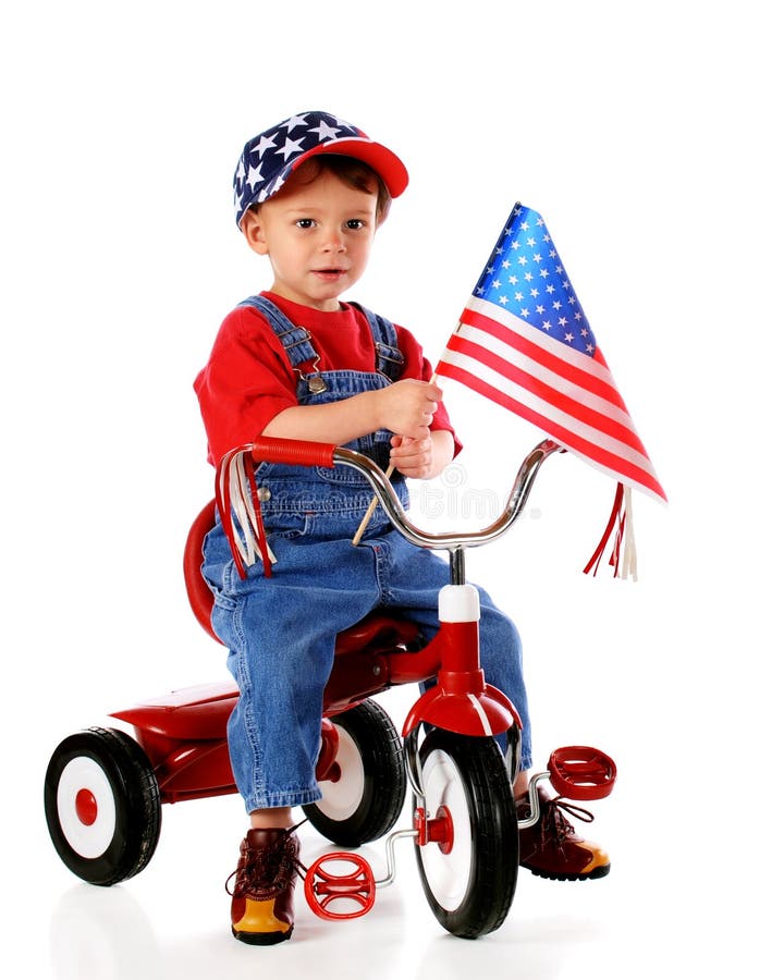 A two-year-old waving an American flag while riding a trike and wearing a stars-and-stripes baseball cap. Isolated on white. A two-year-old waving an American flag while riding a trike and wearing a stars-and-stripes baseball cap. Isolated on white.