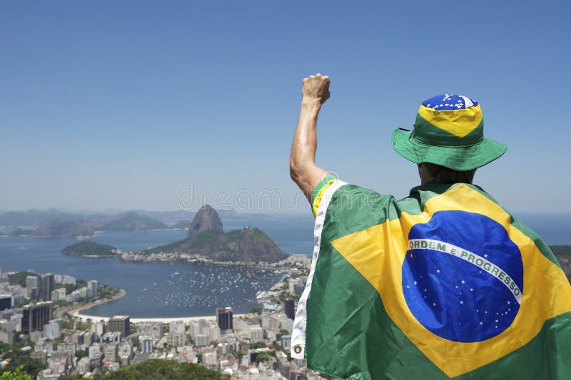 Patriotic Brazilian fan standing wrapped in flag holding up fist pump at Sugarloaf Mountain Botafogo view Rio de Janeiro Brazil. Patriotic Brazilian fan standing wrapped in flag holding up fist pump at Sugarloaf Mountain Botafogo view Rio de Janeiro Brazil