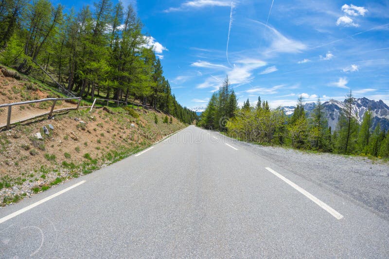 Paved two lane road crossing mountains and forest in scenic alpine landscape and moody sky. Panoramic view from car mounted camera