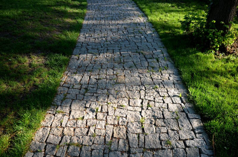 Pavimento de granito de partes irregulares de piedra desbastada alrededor de un parque con césped verde gris del camino peatonal