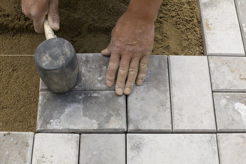 Le mani di un lavoratore manuale di posa di pavimentazione in cemento blocchi.