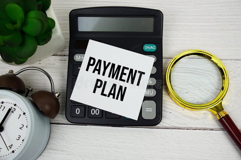 Payment Plan text message on sticky note with magnifying glass, alarm clock and calculator on wooden background stock image
