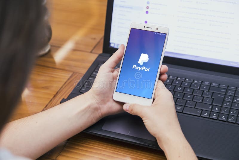 PayPal на экране смартфона Девушка перед ноутбуком с сотовым телефоном стоковые фотографии rf PayPal на экране смартфона Девушка перед ноутбуком с сотовым телефоном стоковые фотографии rf