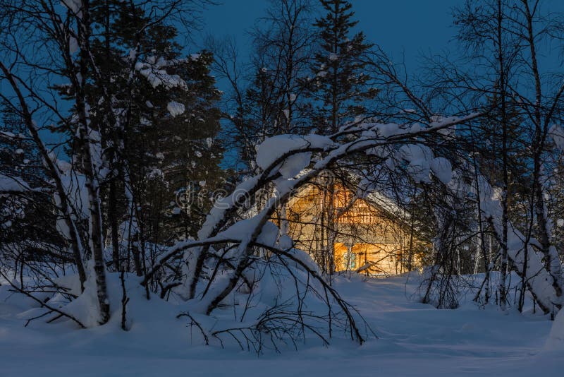 Paysage froid de nuit d'hiver, petite maison en bois avec la lumière chaude images stock Paysage froid de nuit d'hiver, petite maison en bois avec la lumière chaude images stock