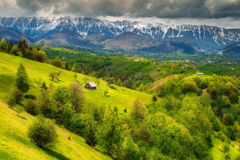 Majestic alpine landscape with stunning green fields and high snowy Piatra Craiului mountains near Brasov, Transylvania, Romania, Europe. Majestic alpine landscape with stunning green fields and high snowy Piatra Craiului mountains near Brasov, Transylvania, Romania, Europe