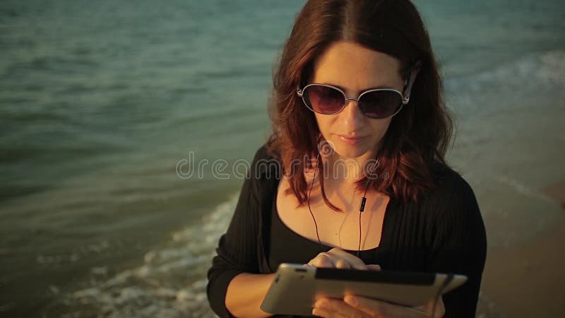 PC de la tableta de las aplicaciones de la mujer en la playa metrajes