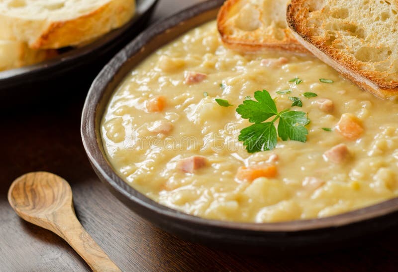 Rustico ciotola con abbondante sputare la zuppa di piselli con prosciutto, carote, patate e pane francese.