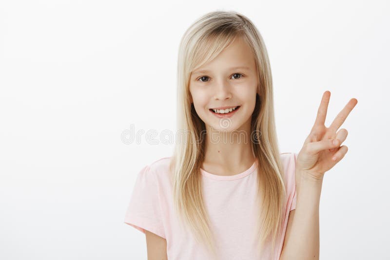 Peace to all my fans. Portrait of adorable fashionable little european girl in pink t-shirt showing victory gesture and