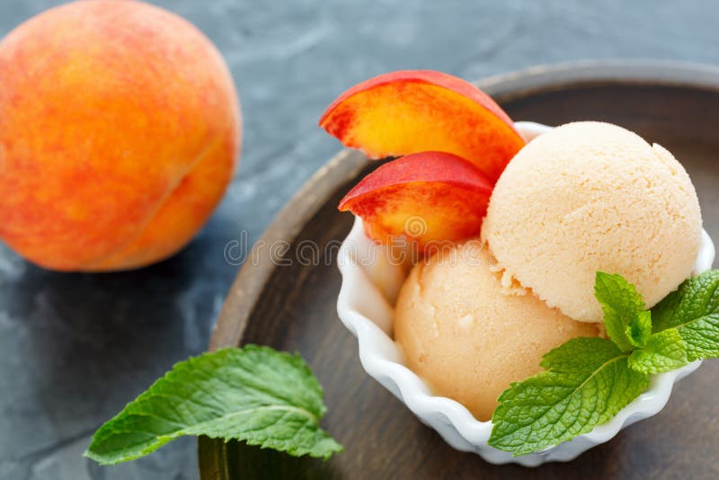 Balls peach ice cream and mint leaves in bowl on wooden plate, selective focus. Balls peach ice cream and mint leaves in bowl on wooden plate, selective focus.