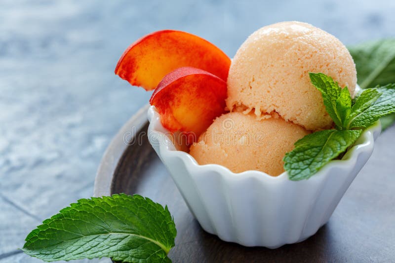 Cup of homemade peach ice cream, fresh peach slices and mint on the wooden plate, selective focus. Cup of homemade peach ice cream, fresh peach slices and mint on the wooden plate, selective focus.