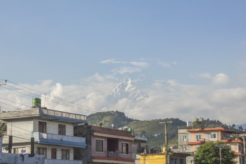 Peak of high mountain with snow sticks out of the clouds above the city stock image Peak of high mountain with snow sticks out of the clouds above the city stock image