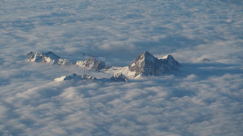 The peaks of the mountains rise out from the clouds that cover the earth. Landscape from the airplane window