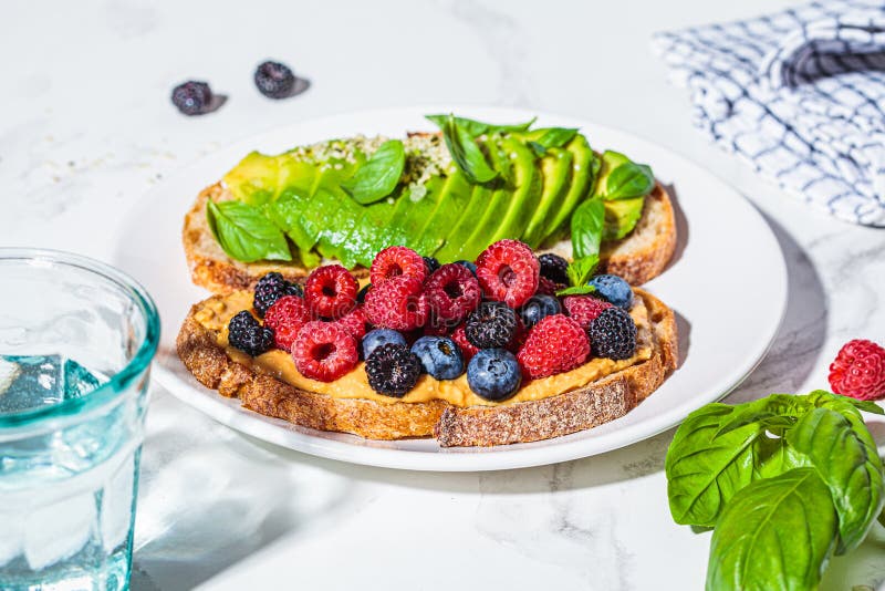 Peanut butter and berries toast and avocado toast with basil on white plate. Healthy vegan breakfast concept