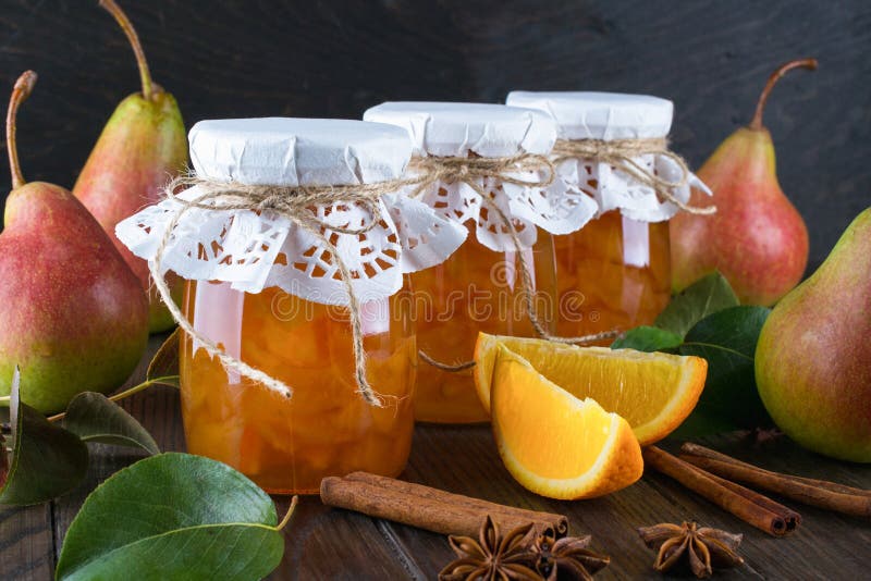 Pear and orange jam in glass jars with ripe pears, cinnamon sticks, anise stars and green leaves