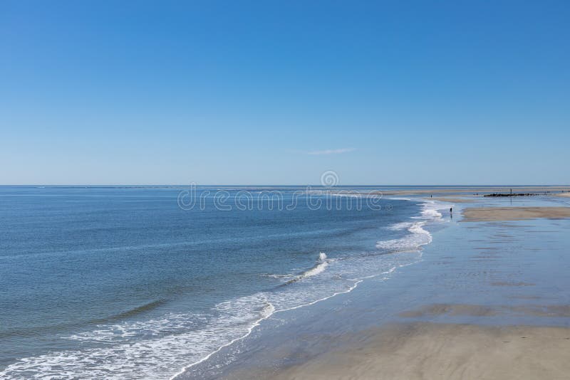 Peatones de playa distantes a lo largo de una playa de arena plana junto al océano aguas tranquilas y cielo azul fotografía de archivo