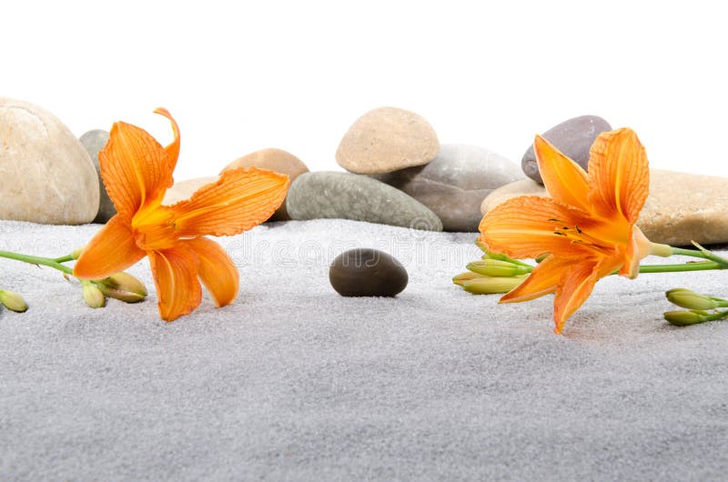 Pebble stones and orange lily flowers on gray sand