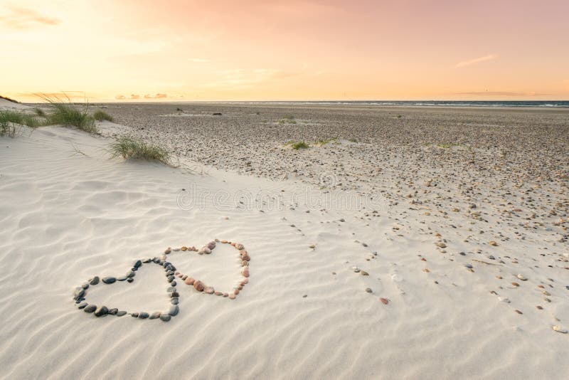 Pebbles arranged in shape of two hearts on sand beach ripples with beautiful sunset.