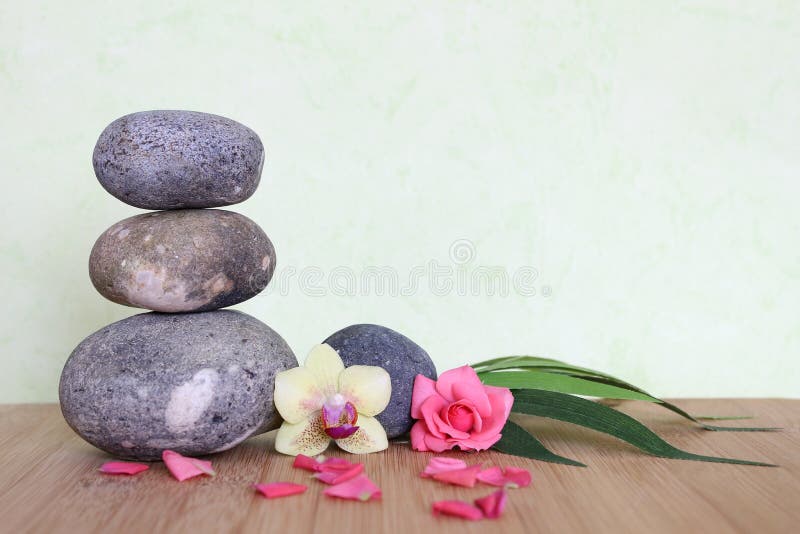 Pebbles stacked in a Zen life fashion on a bamboo wooden board with a pink flower and an orchid on a green background