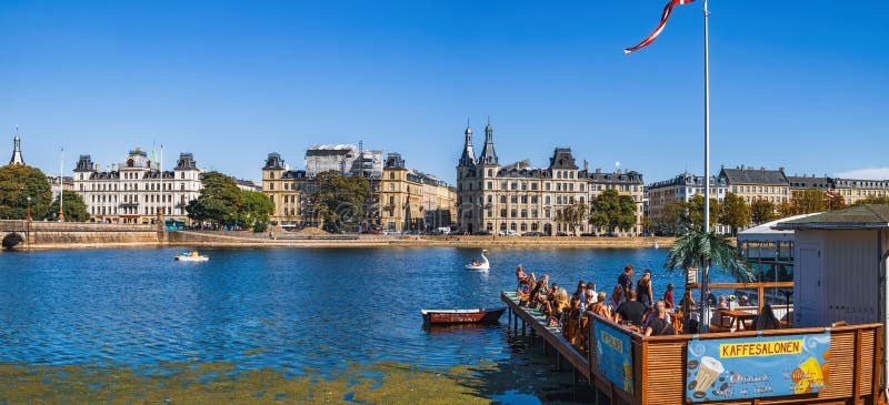 Copenhagen, Denmark - August 7, 2018: Tourists visiting and enjoying views of Queen Louise`s Bridge and Peblinge Lake in central Copenhagen from Kaffesalonen outdoor cafe. Copenhagen, Denmark - August 7, 2018: Tourists visiting and enjoying views of Queen Louise`s Bridge and Peblinge Lake in central Copenhagen from Kaffesalonen outdoor cafe