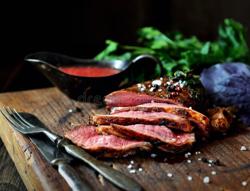 Pedazo de carne asado a la parrilla jugoso en una tabla de cortar, una albahaca, un perejil, especias, un cuchillo del vintage y fotos de archivo libres de regalías Pedazo de carne asado a la parrilla jugoso en una tabla de cortar, una albahaca, un perejil, especias, un cuchillo del vintage y fotos de archivo libres de regalías