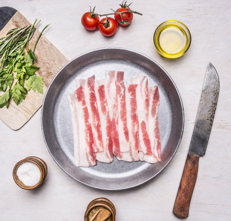 Pedazos apetitosos de tocino crudo en un sartén con clos rústicos de madera de la opinión superior del aceite, apuñalados, de las foto de archivo