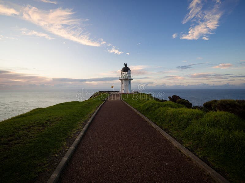 Pedestrian asphalt road walkway leading to historic white Cape Reinga lighthouse on cliff top in Northland New Zealand