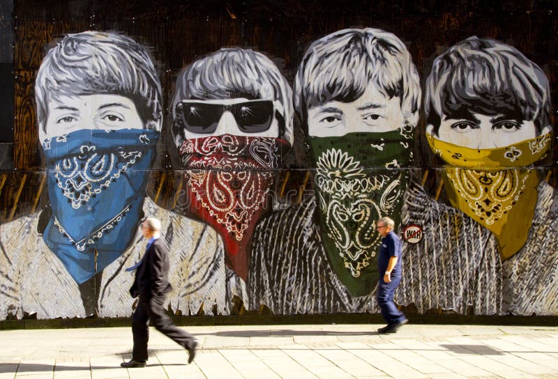 Pedestrians walk past large Beatles graffiti mural