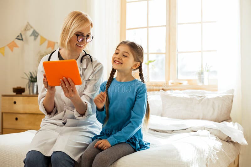 Pediatra de irradiação que ri e que tem o divertimento com uma menina pequena fotos de stock Pediatra de irradiação que ri e que tem o divertimento com uma menina pequena fotos de stock