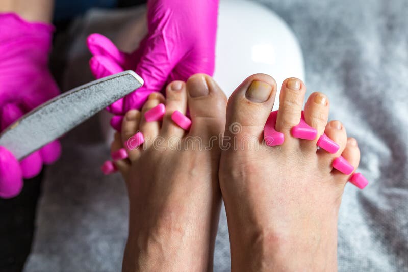 Pedicurist master in pink gloves cuts the cuticle and shellac toe nails in the pedicure salon using drill. Professional pedicure. Fingernail, holding.