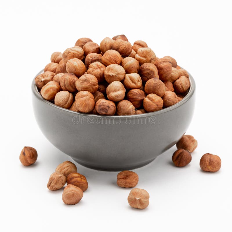 Peeled hazelnuts in a bowl and a few nuts scattered around on a white background