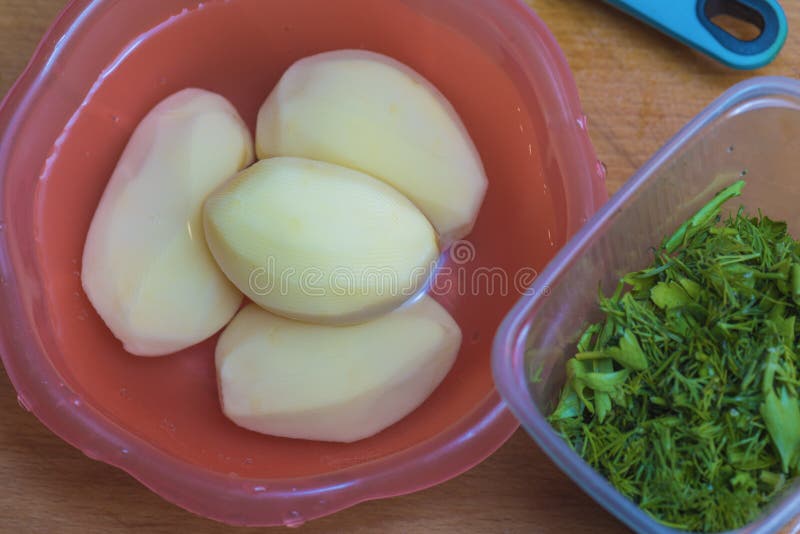 Peeled Potatoes in a Red Bowl of Water and Sliced Greens Stock Photo