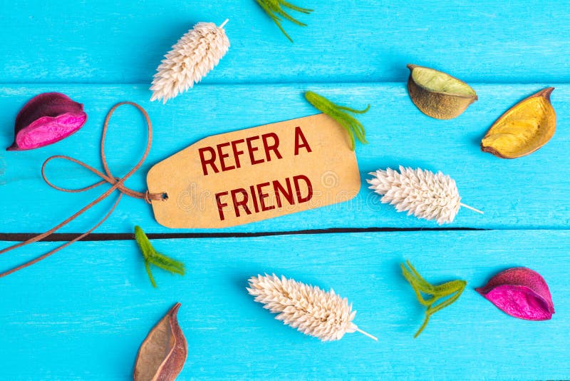 refer a friend text on paper tag with rope and color dried flowers around on blue wooden background. refer a friend text on paper tag with rope and color dried flowers around on blue wooden background
