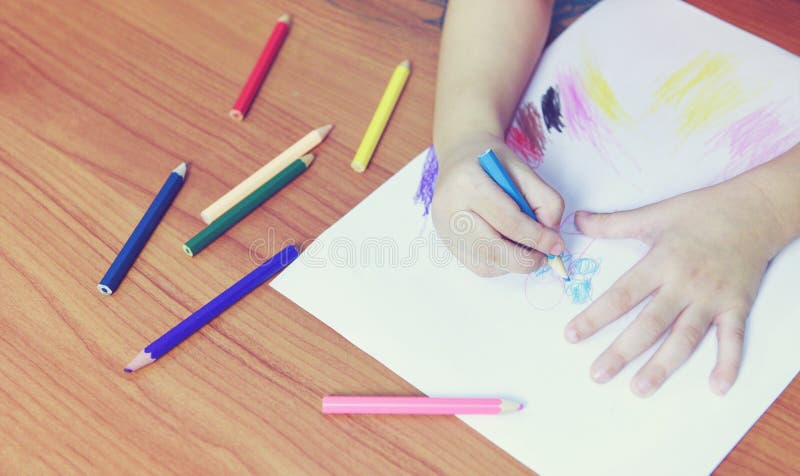 Peinture de fille sur la feuille de papier avec des crayons de couleur sur l'enfant en bois d'enfant de table à la maison - faisa image libre de droits Peinture de fille sur la feuille de papier avec des crayons de couleur sur l'enfant en bois d'enfant de table à la maison - faisa image libre de droits