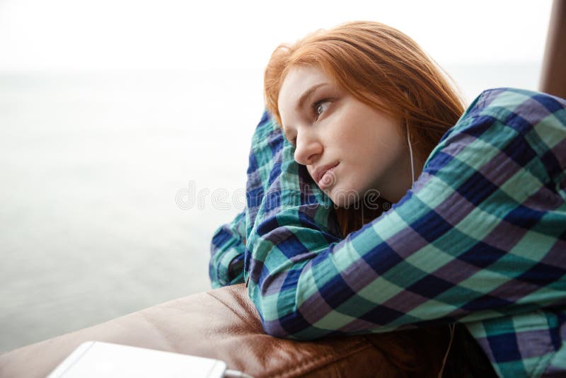 Pensive serene young attractive lady with red hair listening to music and looking away. Pensive serene young attractive lady with red hair listening to music and looking away