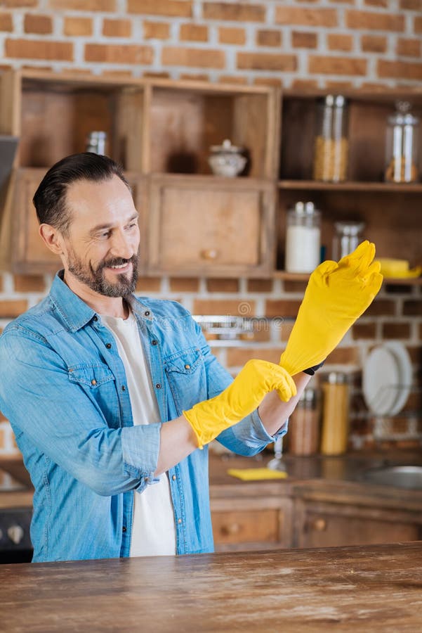 Peinzende mannelijke reinigingsmachine die op gele handschoenen zetten royalty-vrije stock foto's Peinzende mannelijke reinigingsmachine die op gele handschoenen zetten royalty-vrije stock foto's