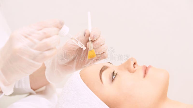 Pelle di pulizia del fronte della giovane donna in salone Buccia del retinolo con la spazzola Sbucciatura organica acida