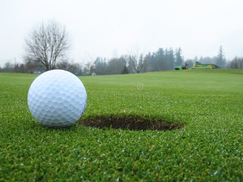 Photo of golf ball beside the hole on the green. Photo of golf ball beside the hole on the green.