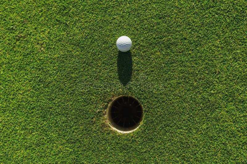 golf ball on green grass with hole and sunlight, lawn, object, cut, putting, equipment, playing, landscape, empty, point, natural, ground, lifestyle, shot, hobby, golf-hole, vacation, clear, meadow, concept, pitch, club, game, nature, field, background, outdoor, closeup, summer, competition, golfing, sport, leisure, course. golf ball on green grass with hole and sunlight, lawn, object, cut, putting, equipment, playing, landscape, empty, point, natural, ground, lifestyle, shot, hobby, golf-hole, vacation, clear, meadow, concept, pitch, club, game, nature, field, background, outdoor, closeup, summer, competition, golfing, sport, leisure, course